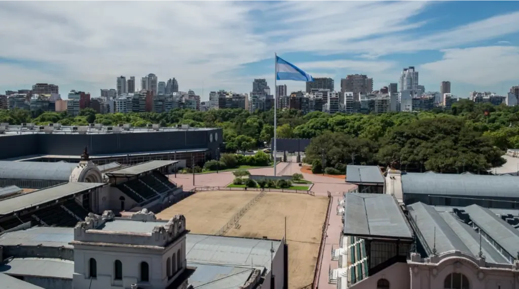 Predio ferial de la rural de la ciudad de buenas aires, imagen con árboles pabellones y la bandera en un mastil en el centro.
